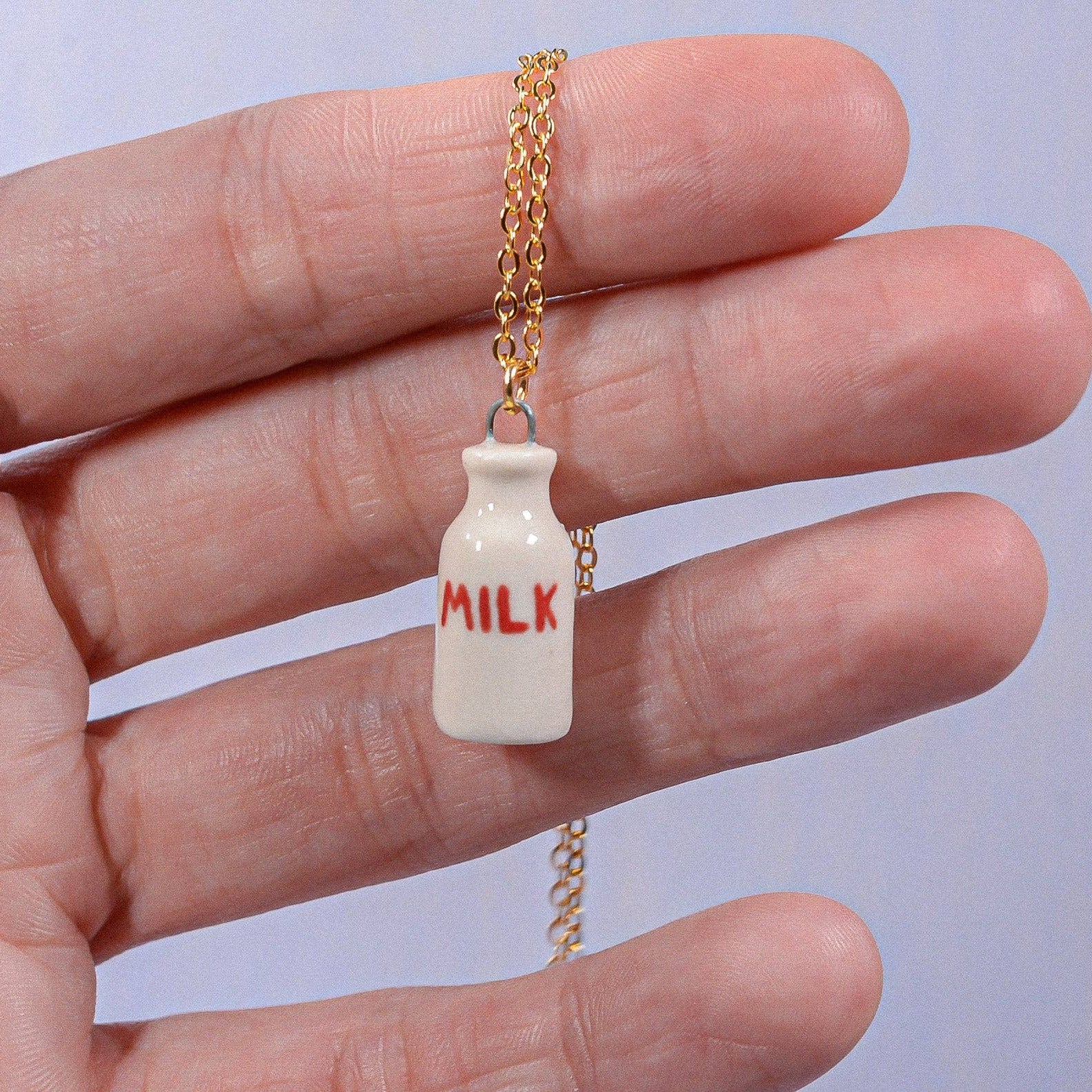 Miniature milk bottle pendant on a chain held in a hand against a light background