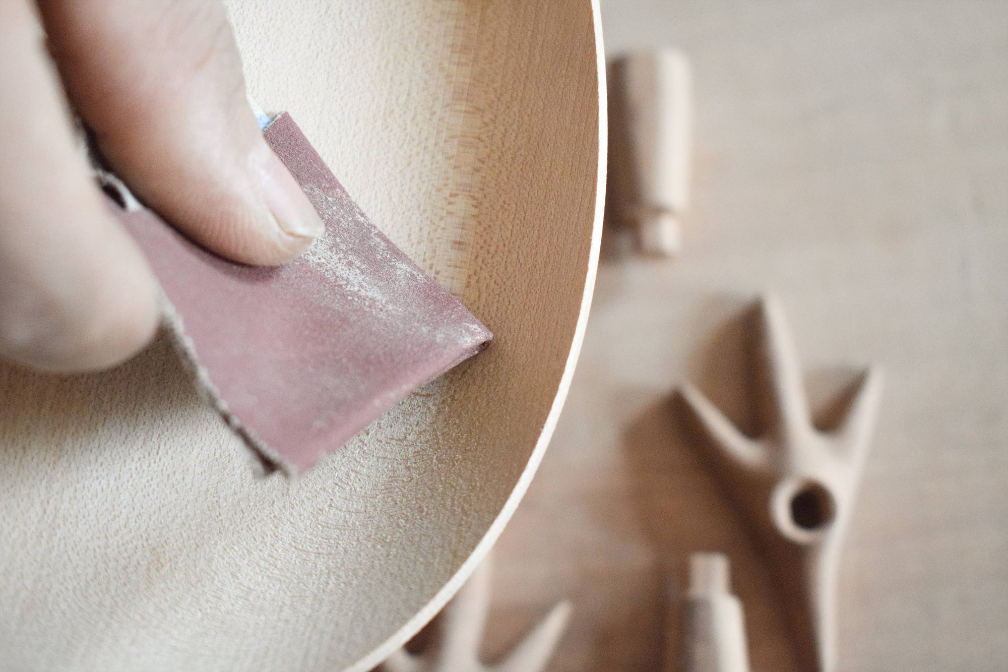 Person sanding a wooden surface with a sanding block, surrounded by sanding tools.