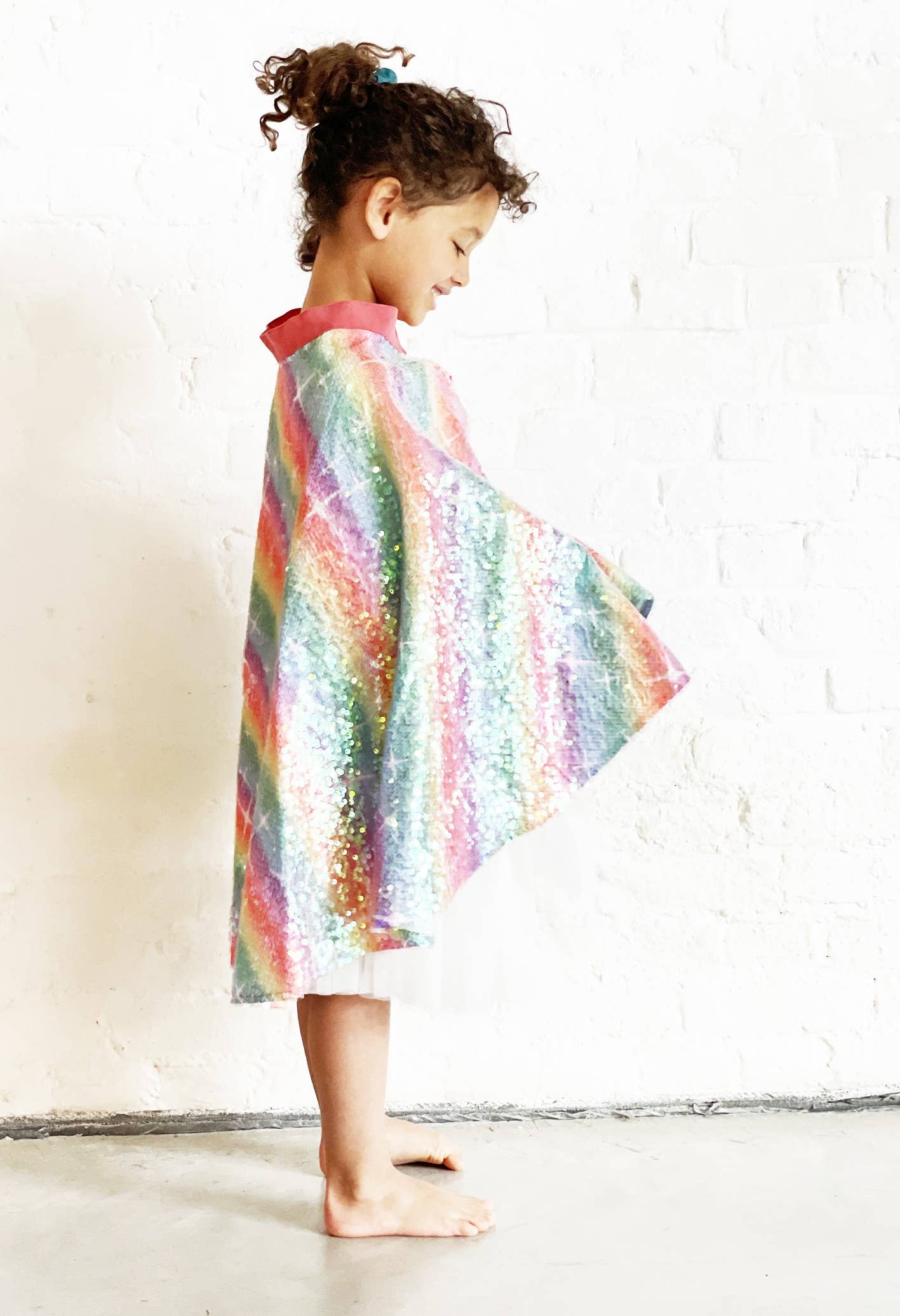 Child wearing a colorful rainbow-patterned dress against a white brick wall.