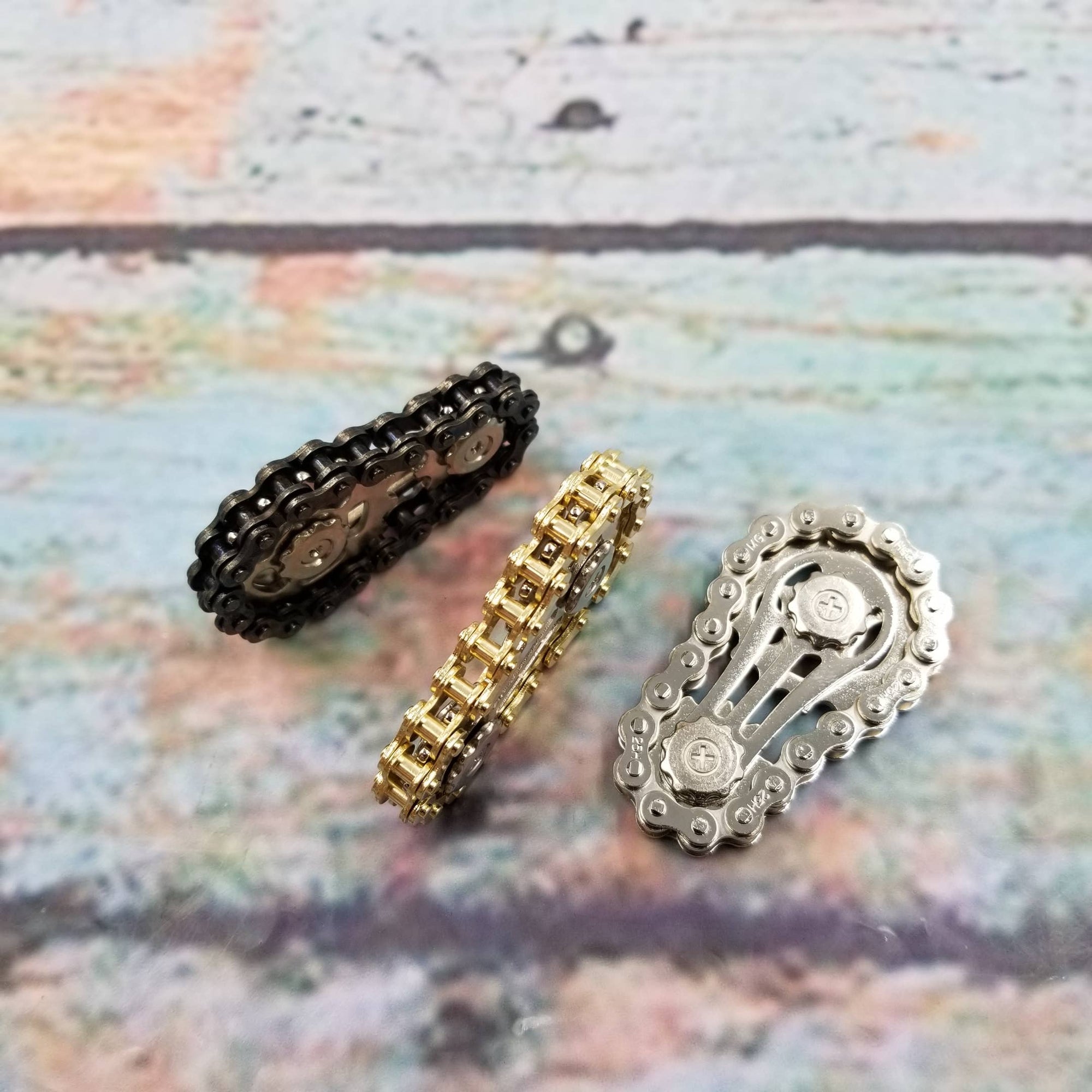 Three motorcycle chains in black, gold, and silver on a textured surface