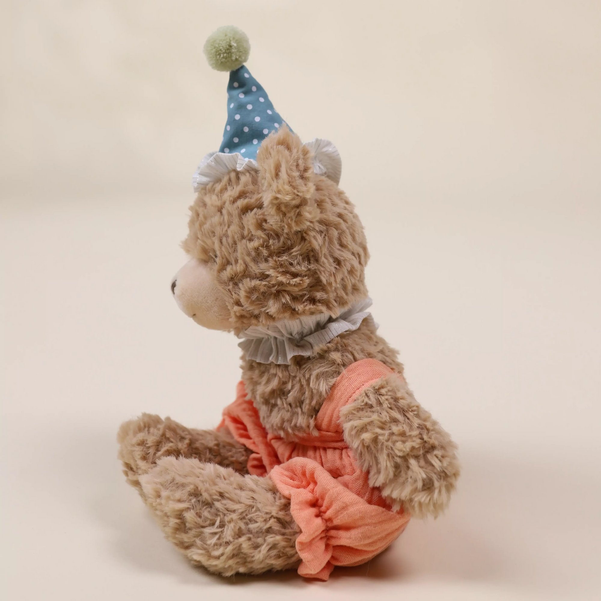 Teddy bear wearing a blue polka dot hat and pink outfit on a beige background