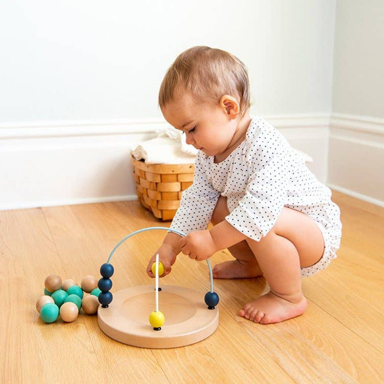 Baby playing with a colorful wooden toy on a wooden floor.