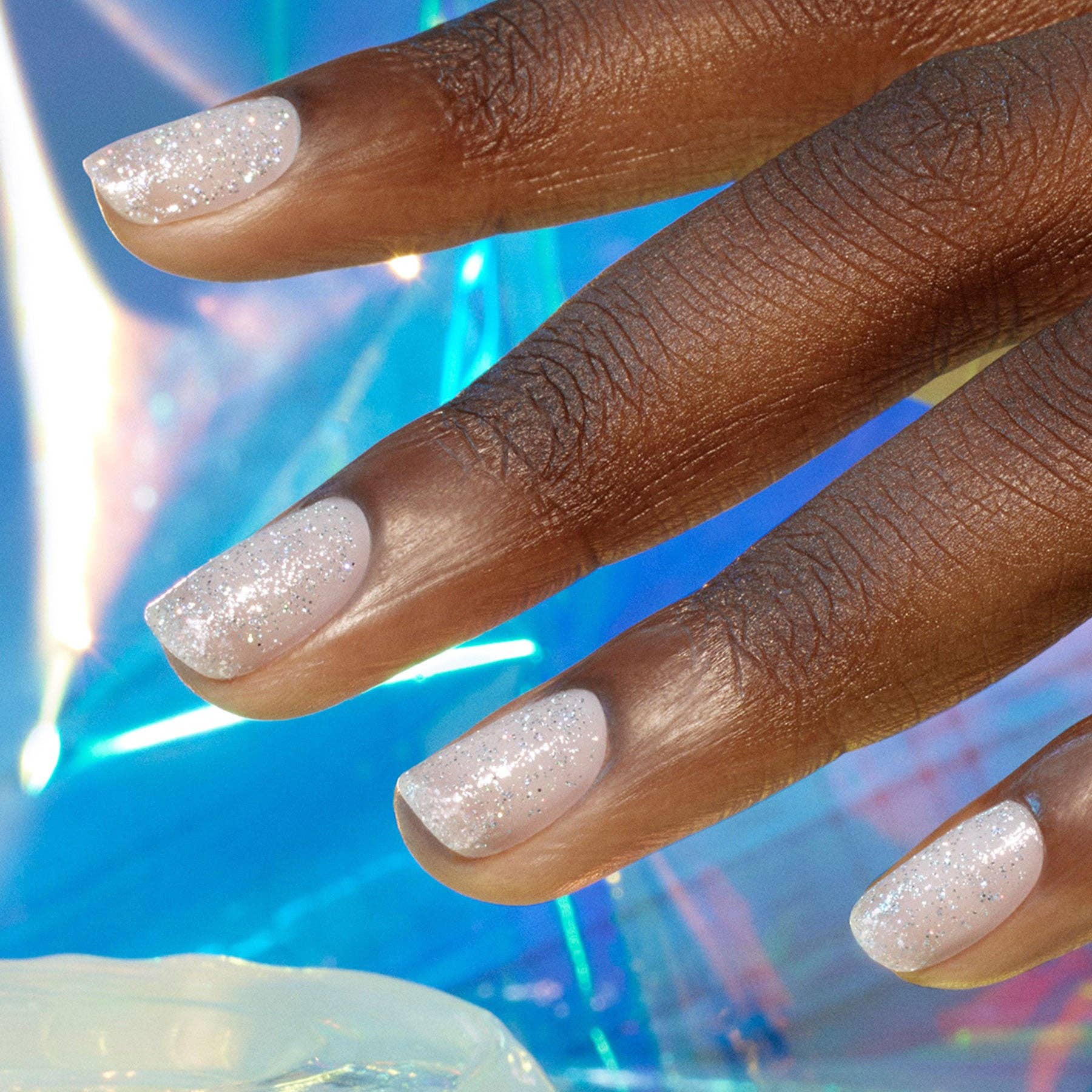 Close-up of a hand with glittery white nail polish against a colorful, blurred background