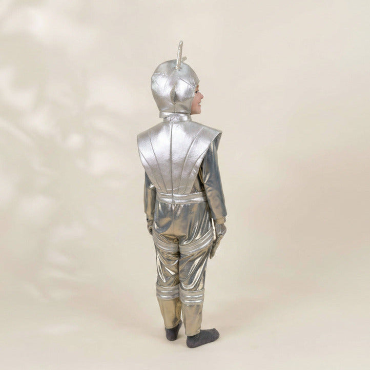 A child wearing a shiny metallic silver futuristic bodysuit or costume, shown from the back against a plain warm beige studio background.