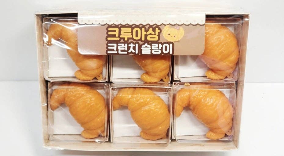 A boxed set of six novelty croissant-shaped items in clear plastic compartments, with a beige header card showing Korean text and a small bear illustration.