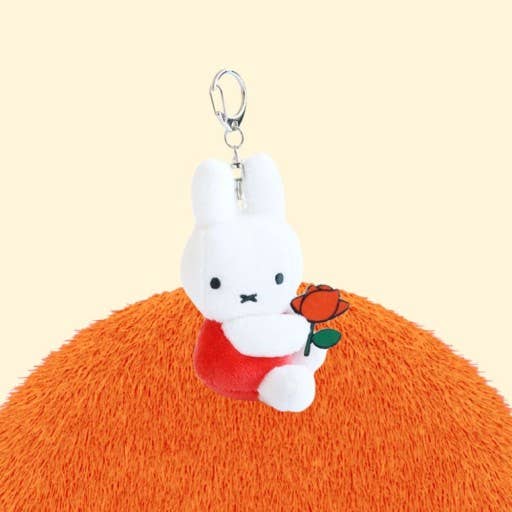 Plush keychain of a white rabbit holding an orange flower on a beige background