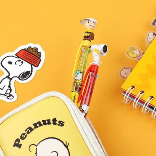 Peanuts-themed stationery items including a pen, notebook, and stickers on a yellow background.