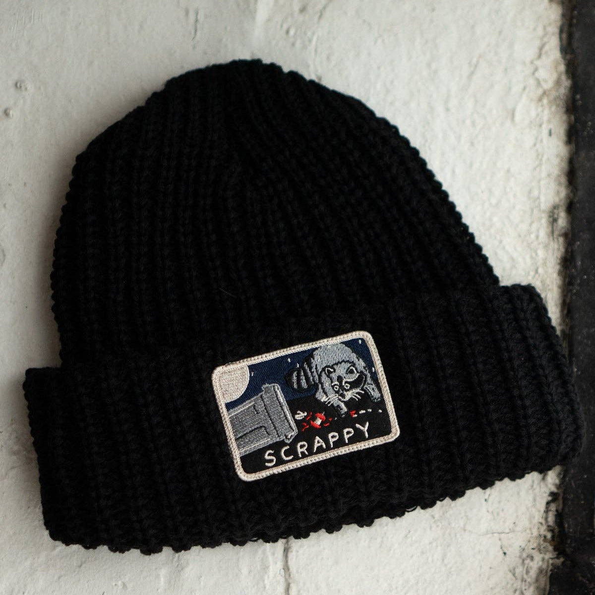 Black beanie with a patch featuring a dog and text on a textured white background