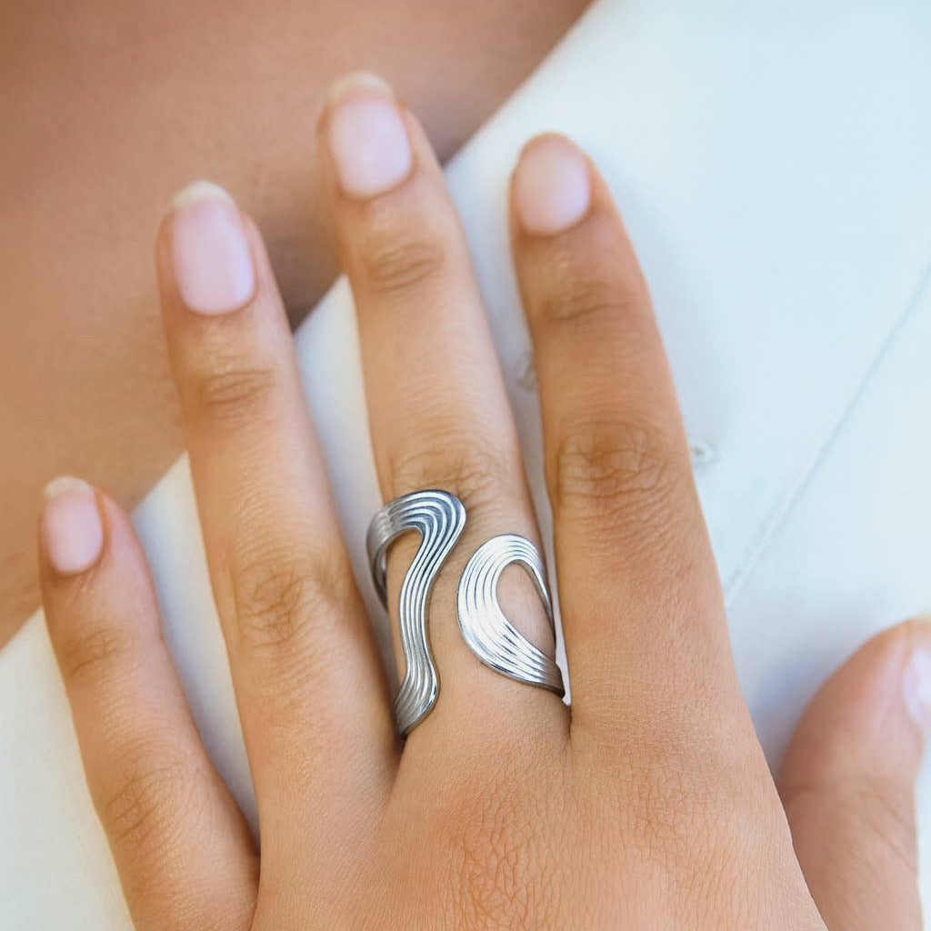 Silver wave-patterned ring on a hand with a white background