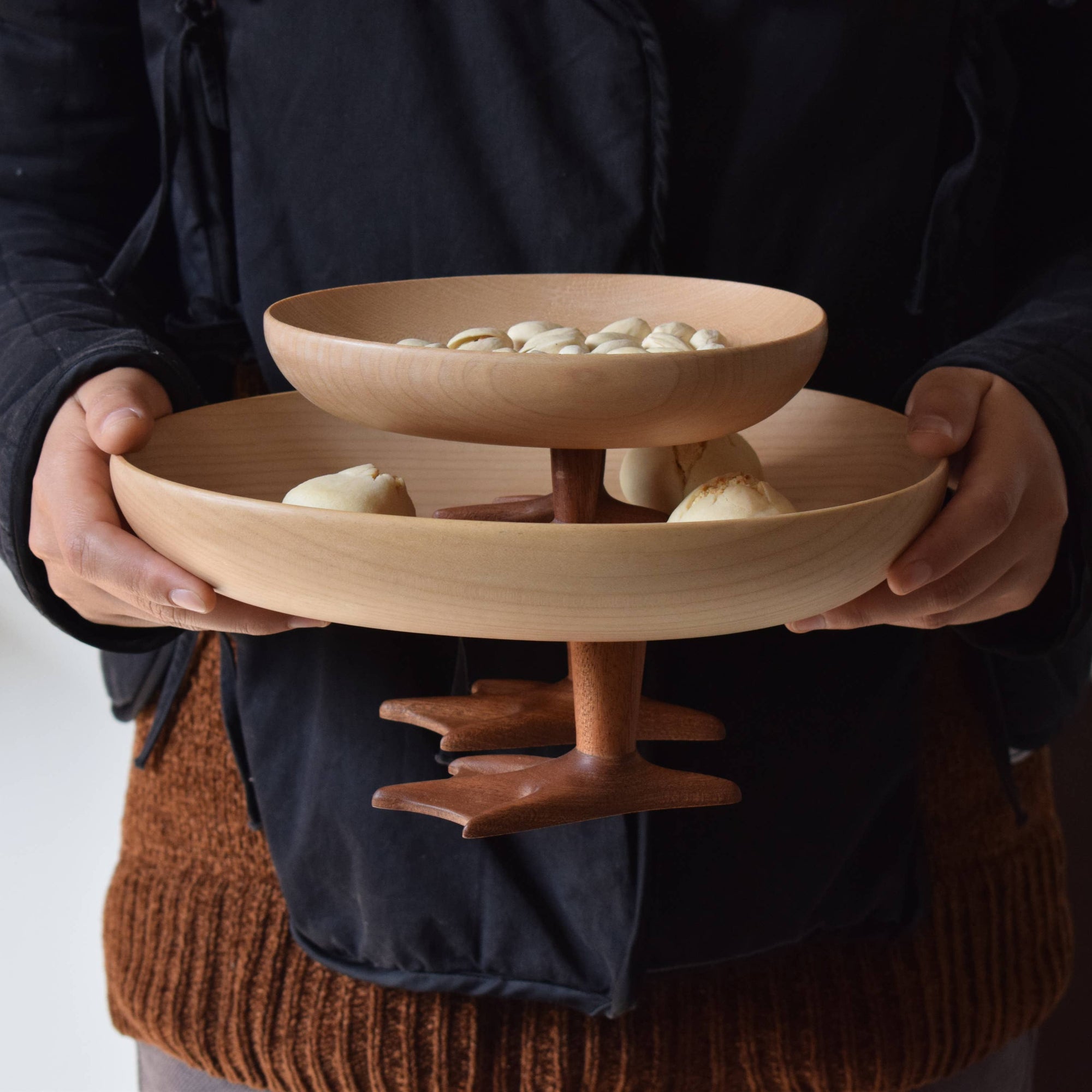 Person holding two-tierd wooden bowls with food items on a plain background