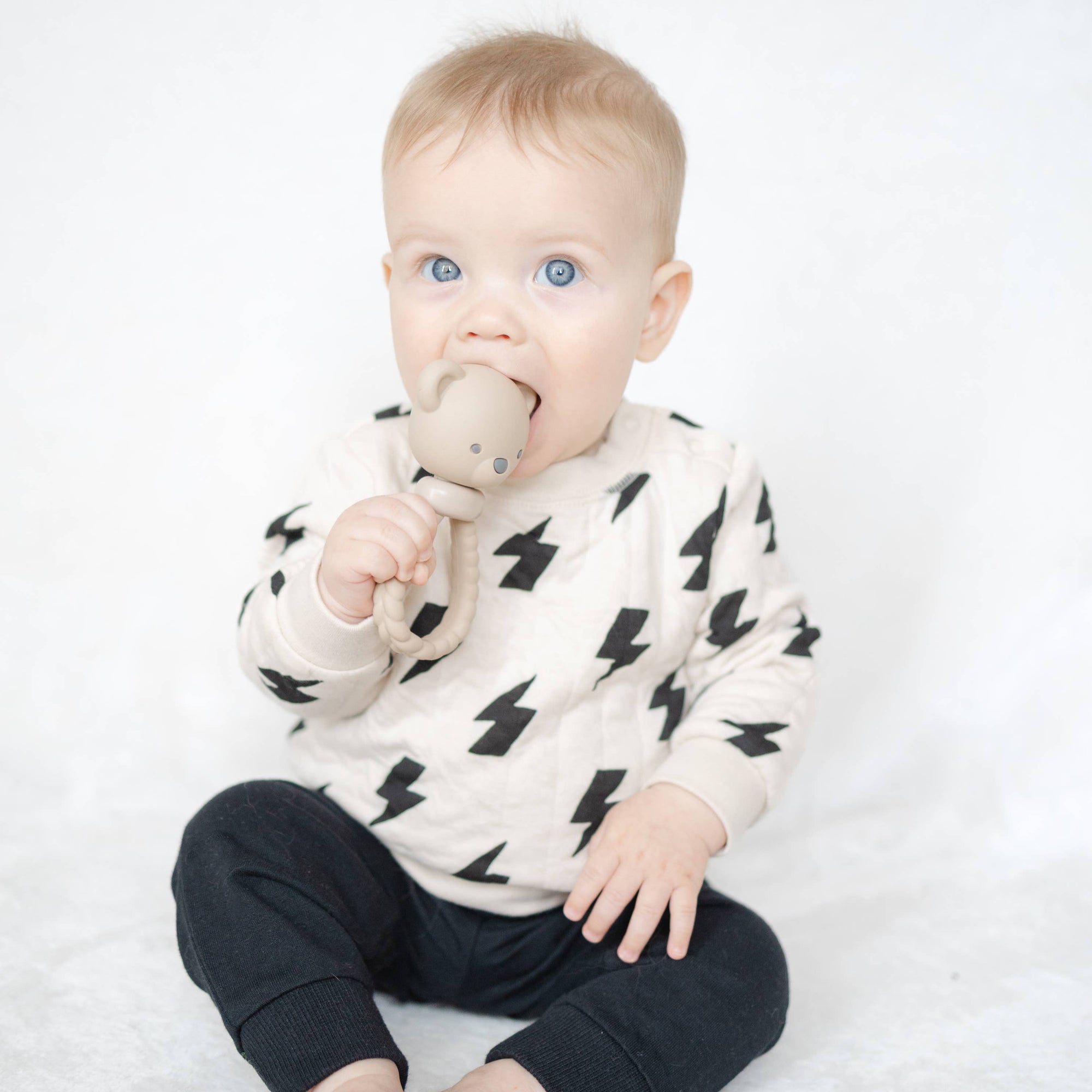 Baby sitting on a white surface wearing a black and white outfit with a teething toy.