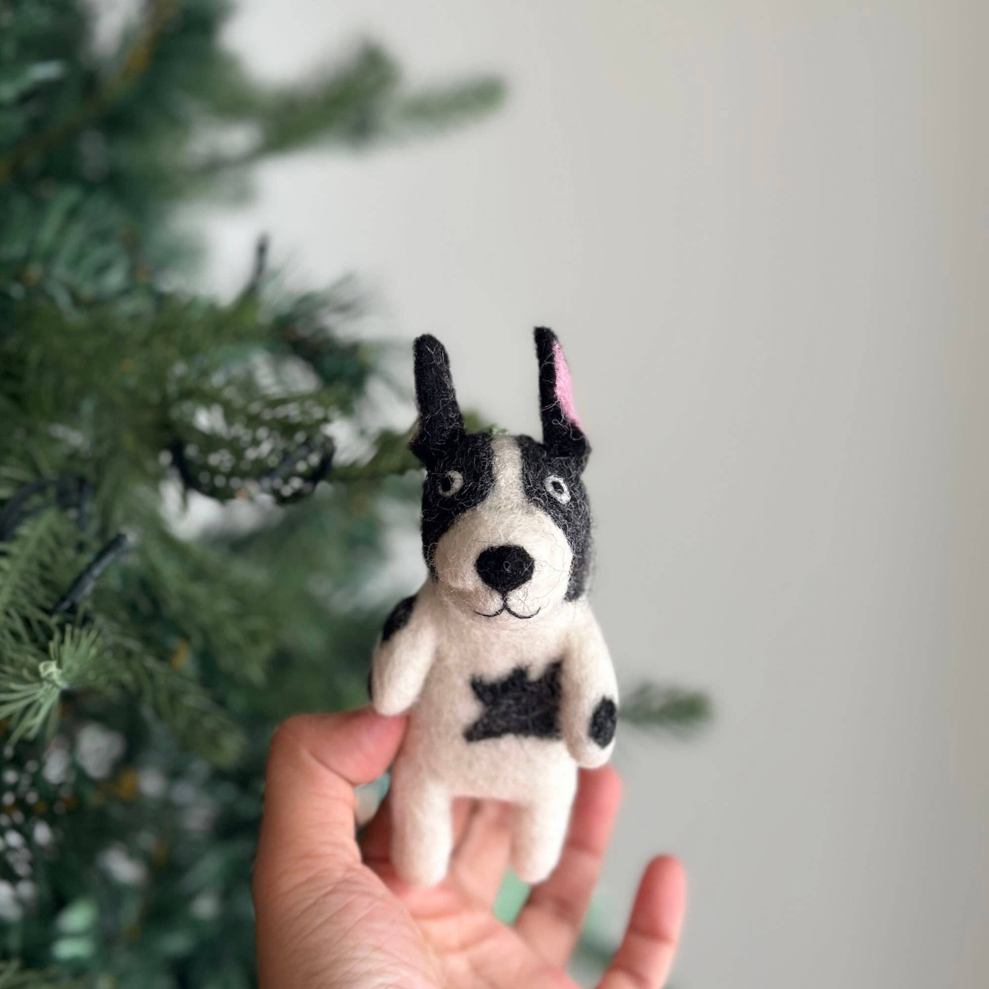 Hand holding a small black and white dog toy in front of a Christmas tree.