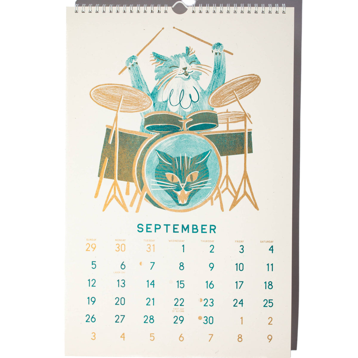A September desk calendar page featuring a stylized illustration of a blue cat playing a drum set, with the word September and a grid of dates below on a white background.