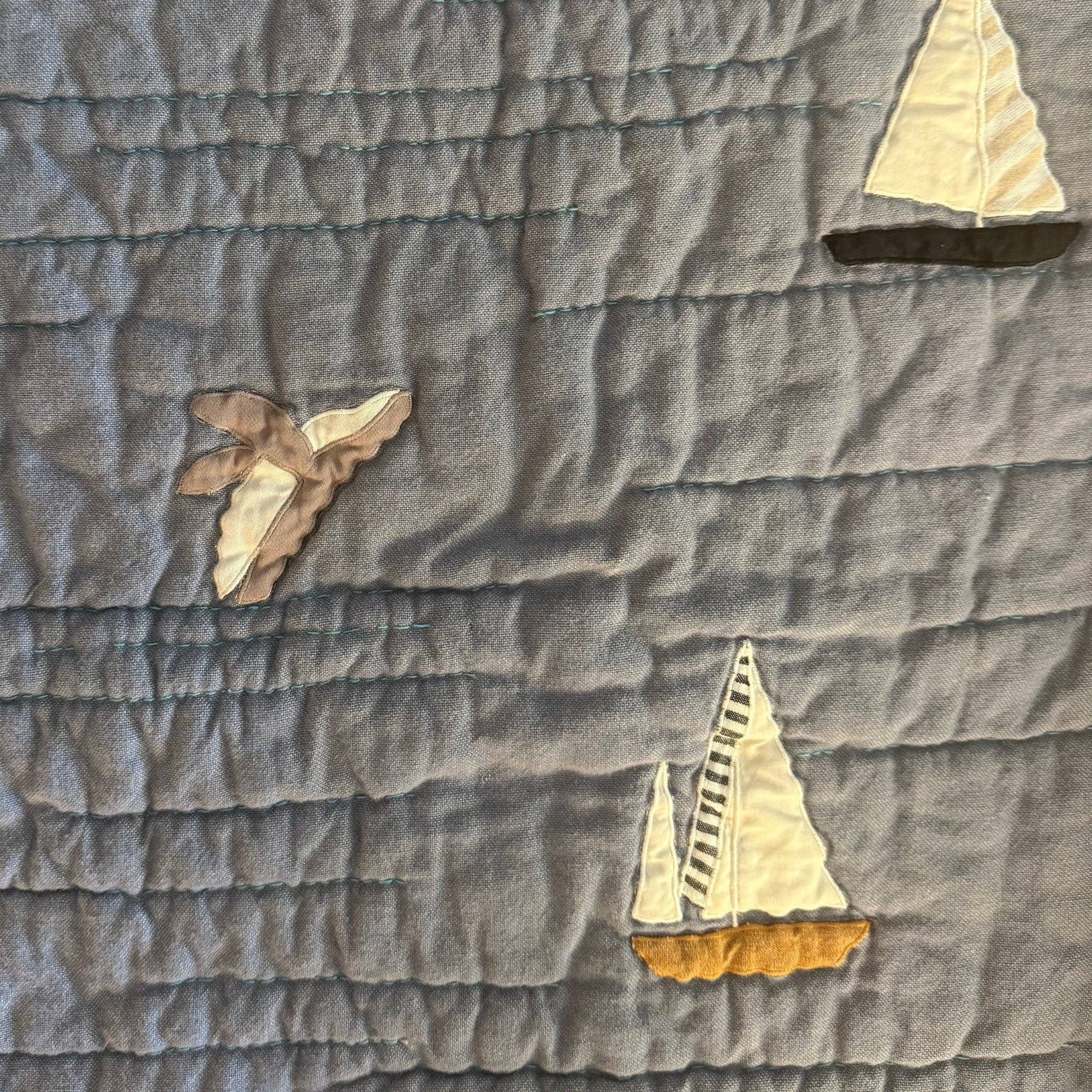 Gray quilt with sailboat appliqués on a textured fabric background