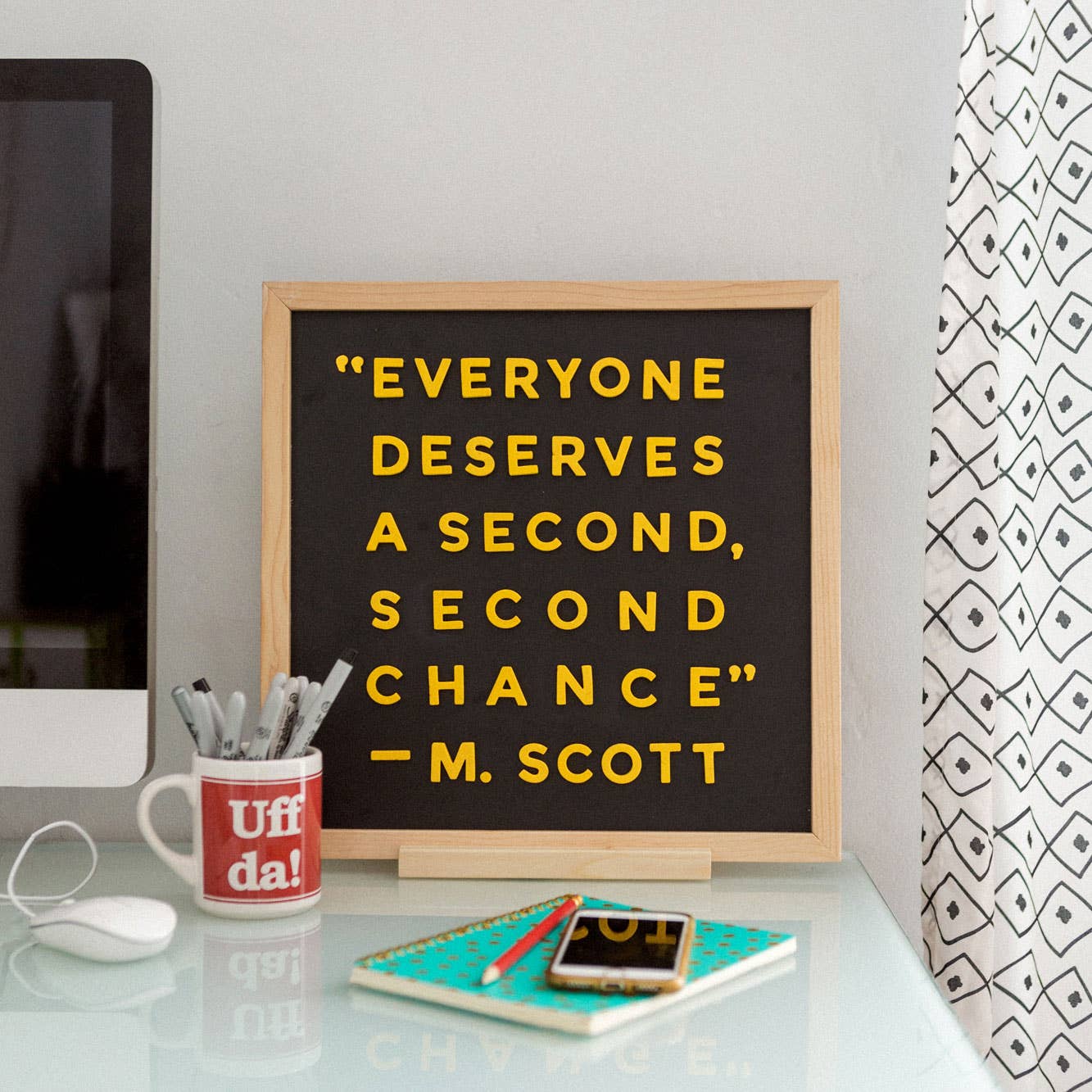 Decorative sign with motivational quote on a desk with office supplies.