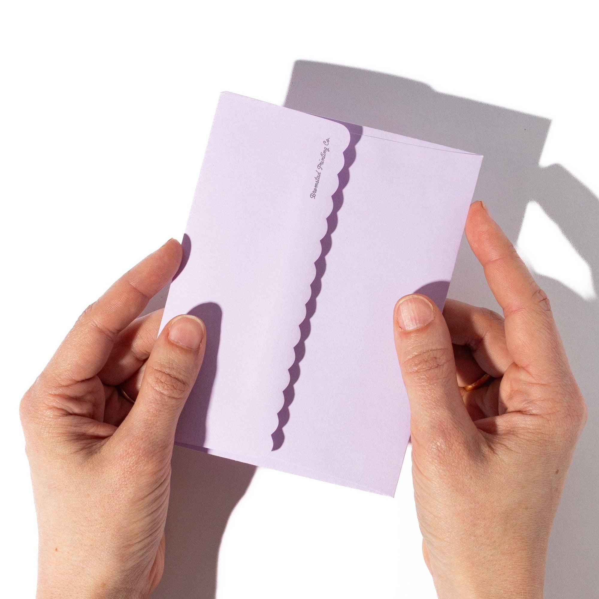 Hands holding a purple greeting card with a white envelope on a light gray background