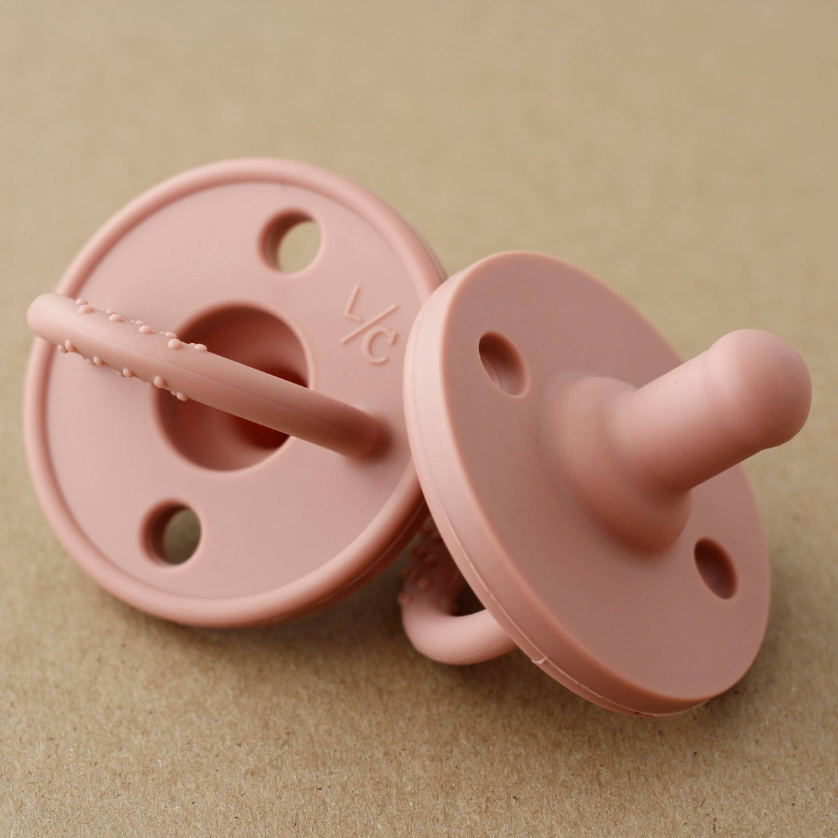 Two pink pacifiers on a beige background