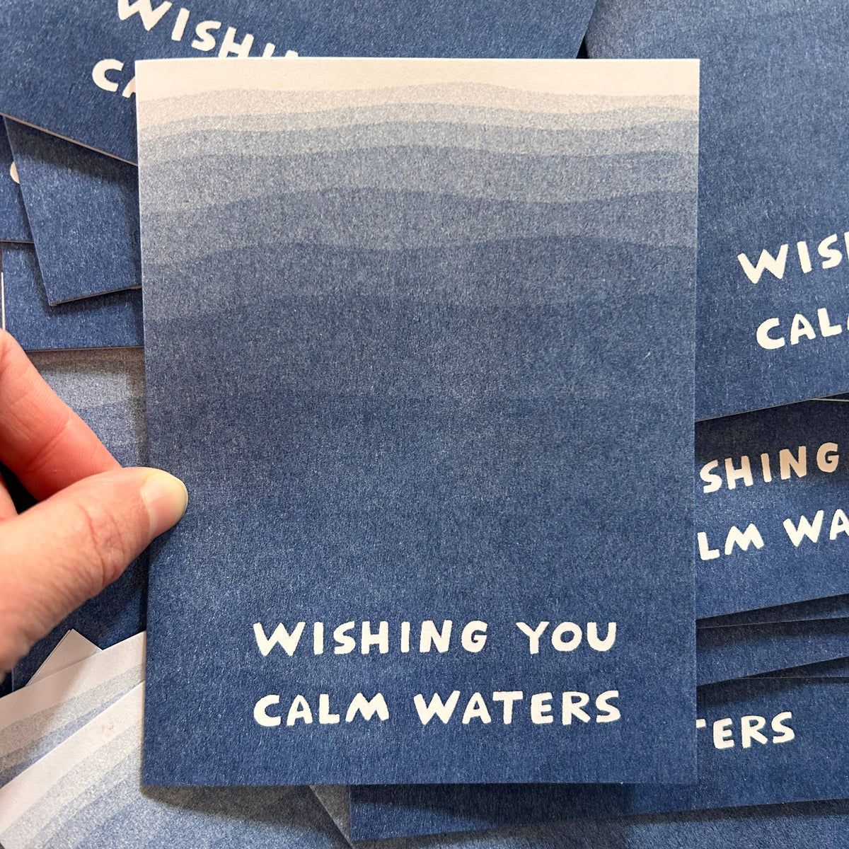 Blue card with 'Wishing You Calm Waters' text held by a hand, surrounded by more cards.