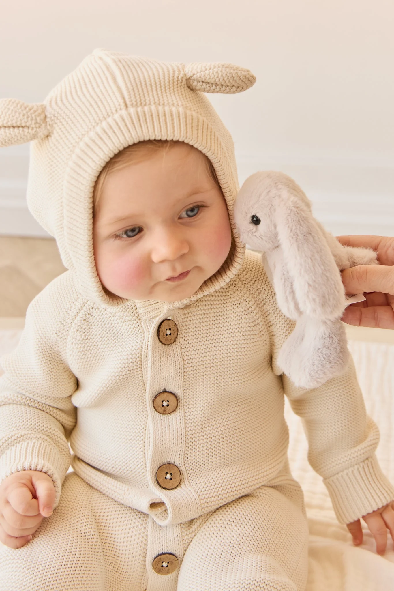 Baby in a cream-colored bunny costume holding a plush toy