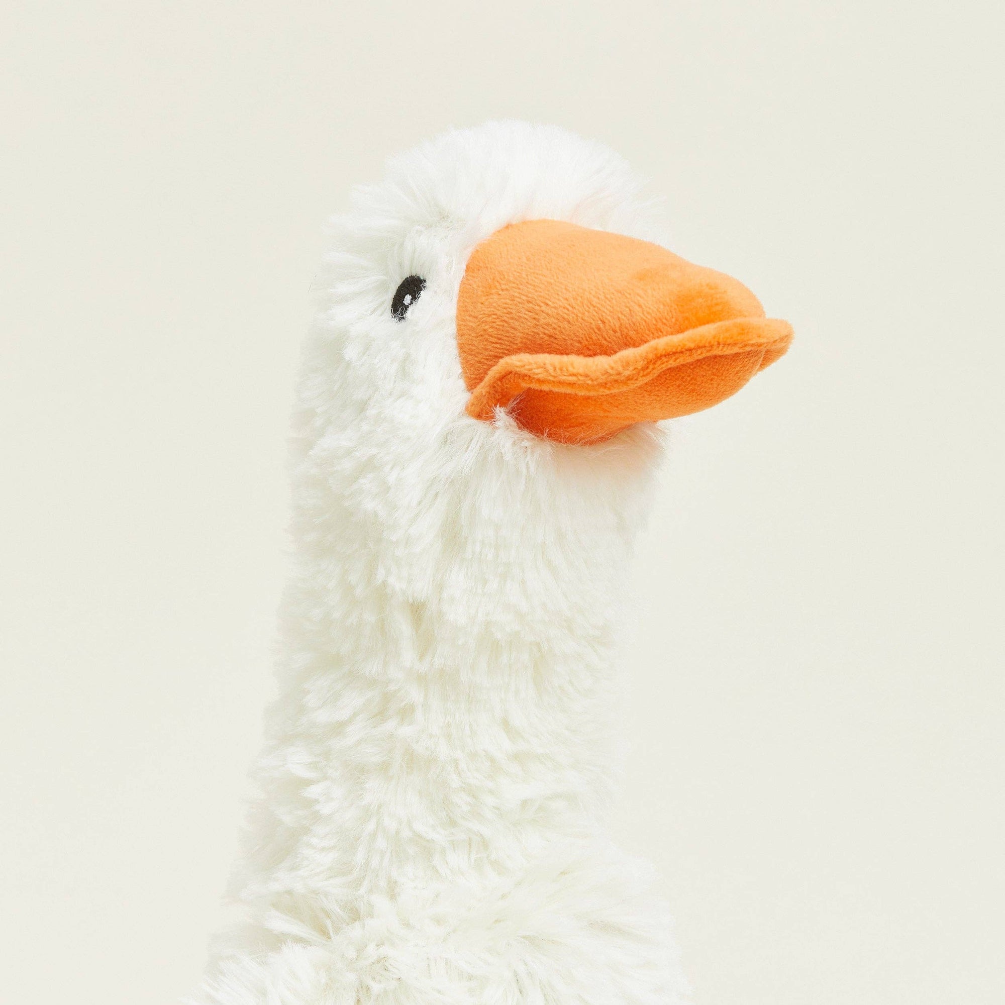 Close-up of a white plush duck toy with an orange beak on a beige background