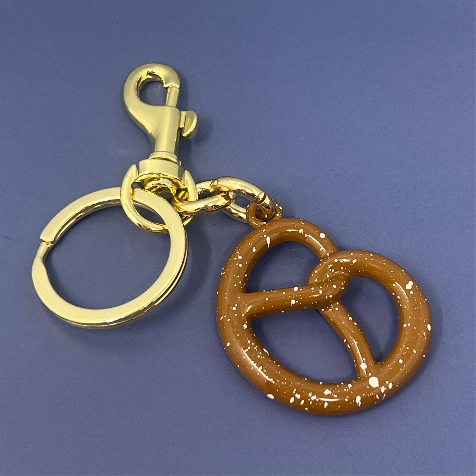Gold keychain with a brown pretzel-shaped charm on a blue background
