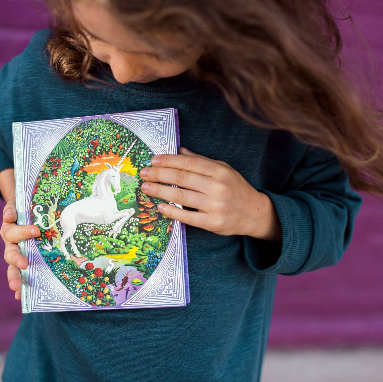 Person holding a coloring book with a unicorn illustration against a purple background