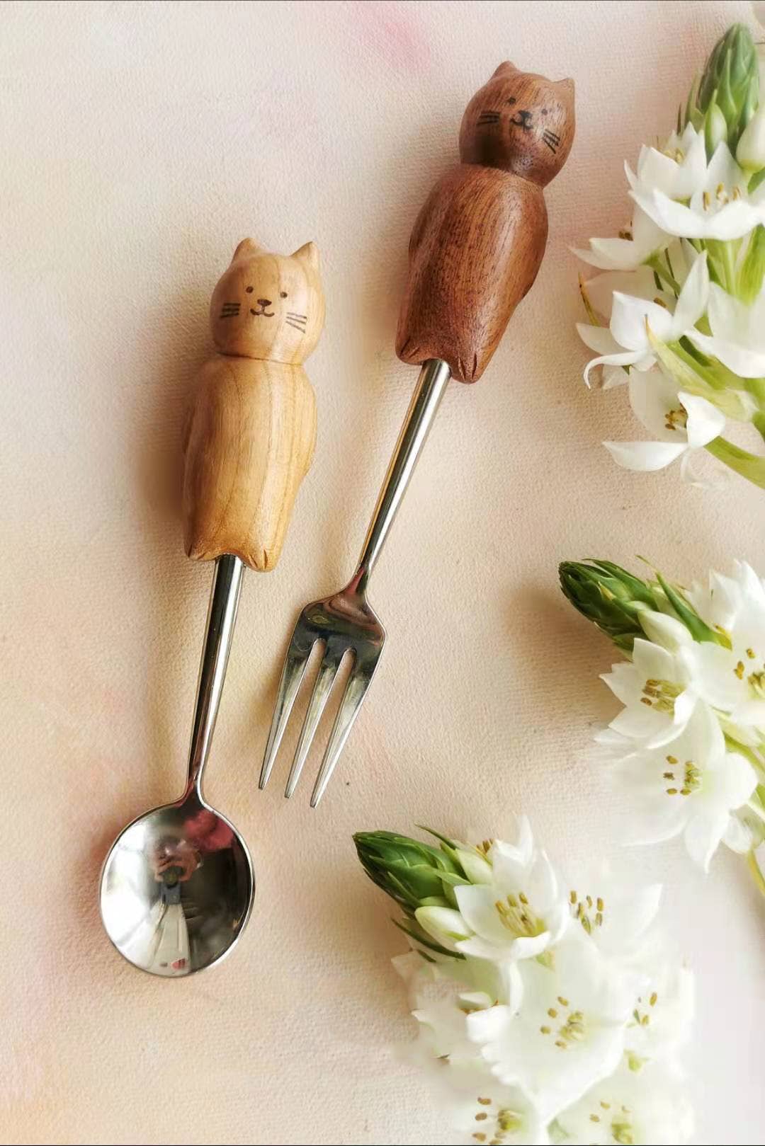 Wooden-handled fork and spoon with cat designs on a light background with flowers.
