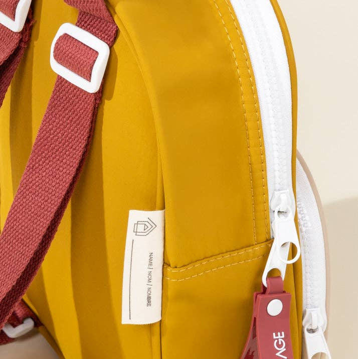 Yellow bag with red strap and 'Coco Village' tag on a beige background