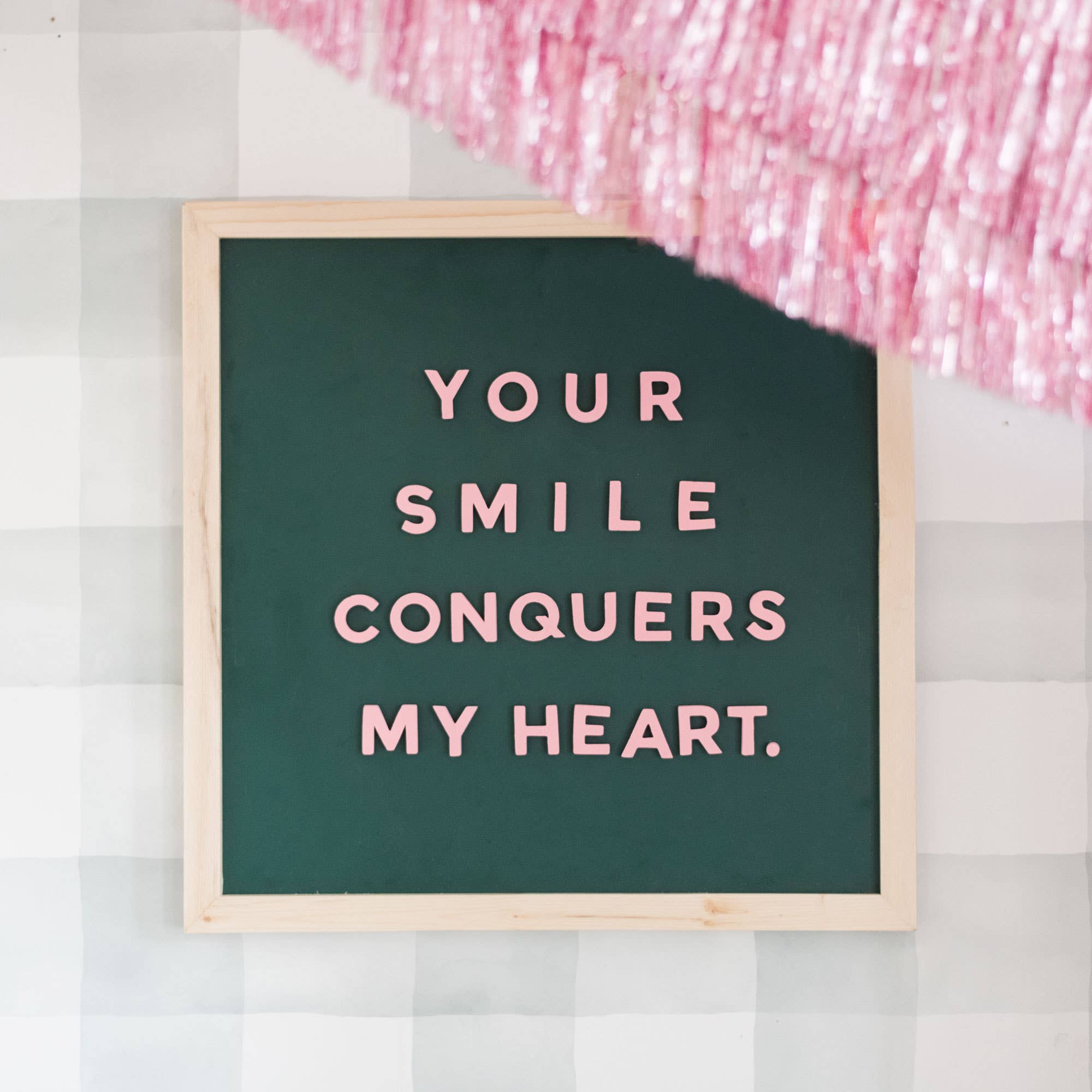 Framed sign with 'Your smile conquers my heart' text on a checkered background