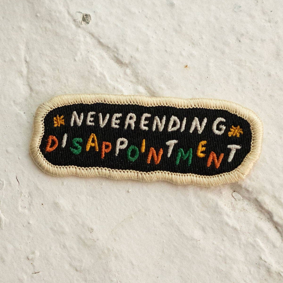 Embroidered patch with 'Neverending Disappointment' text on a textured white background