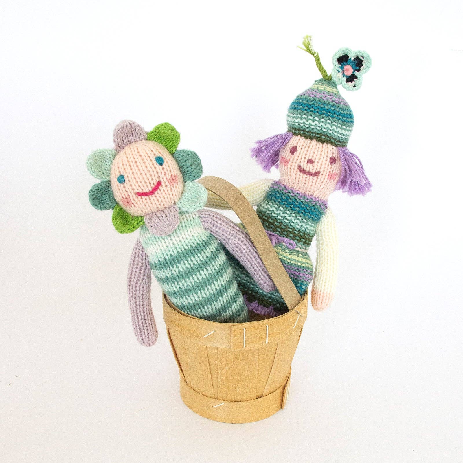 Two knitted dolls with floral and striped designs in a wooden basket on a white background