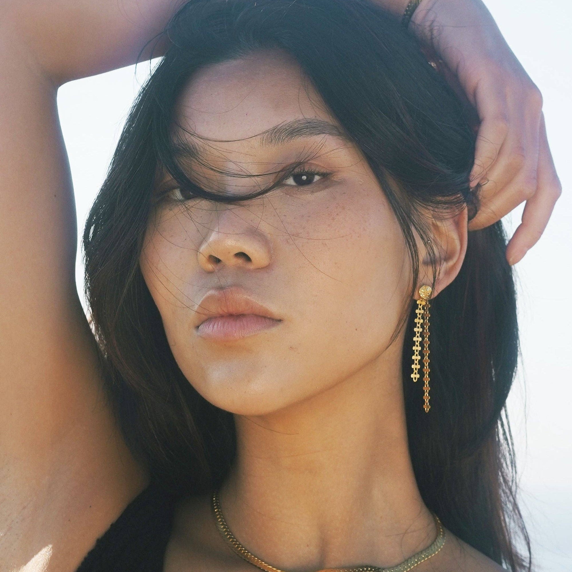 Woman with long dark hair and gold earrings against a light background