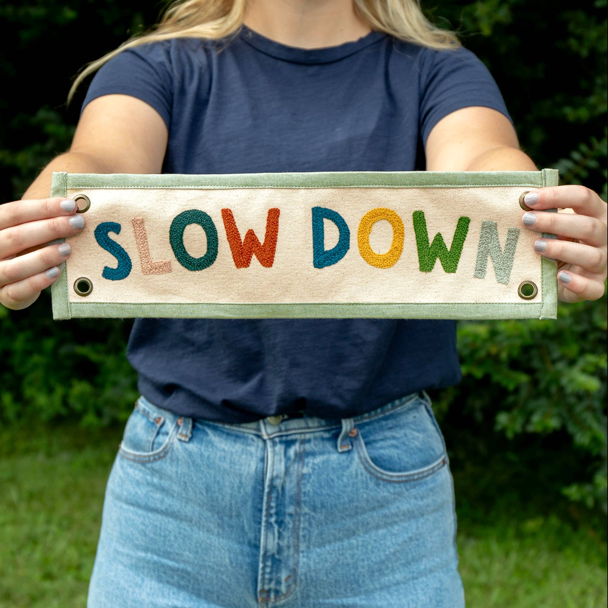 Person holding a sign with 'SLOW DOWN' in colorful letters against a natural background
