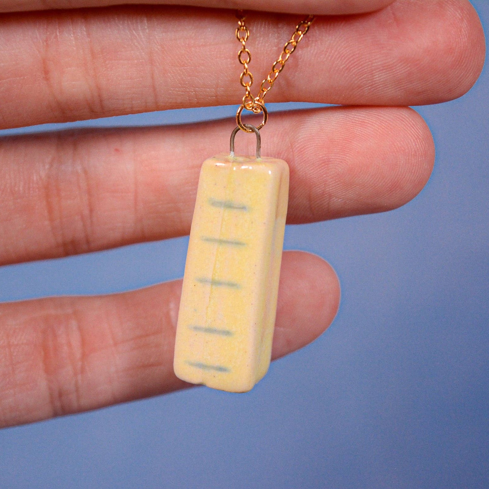 Hand holding a small yellow rectangular pendant with a blue background