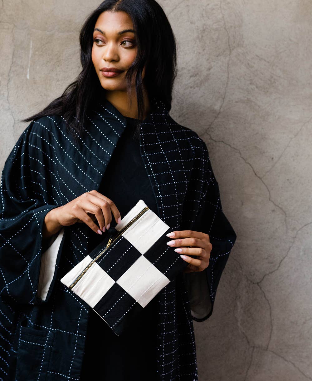 Woman holding a black and white checkered clutch against a textured wall.