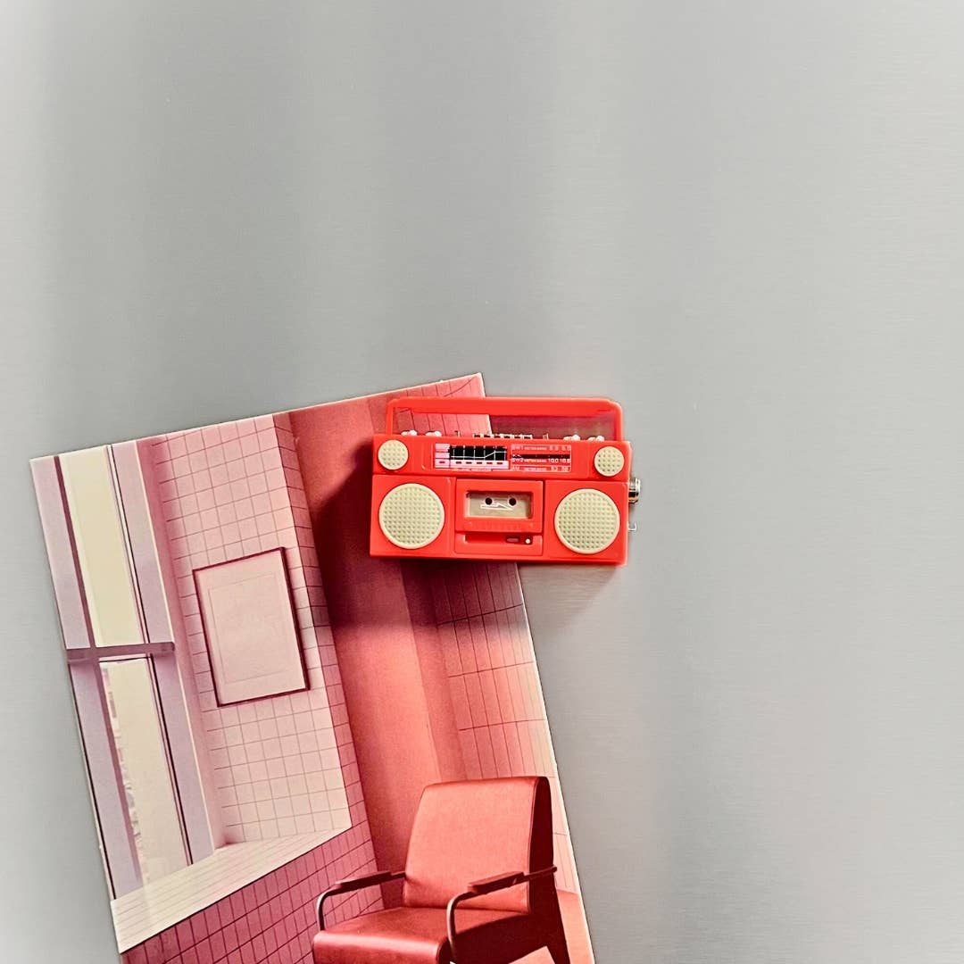 Red boombox on a pink tiled wall with a chair below
