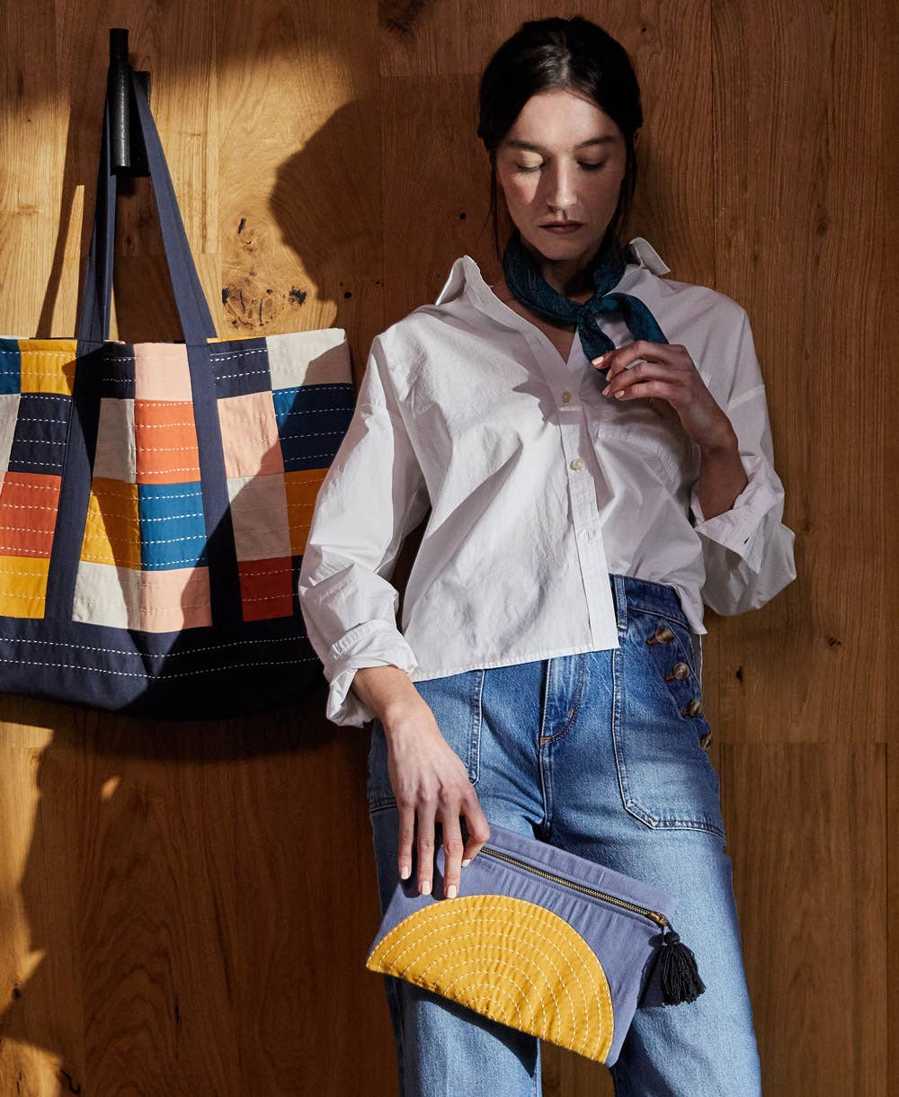 Woman holding a yellow and gray clutch with a colorful bag in the background