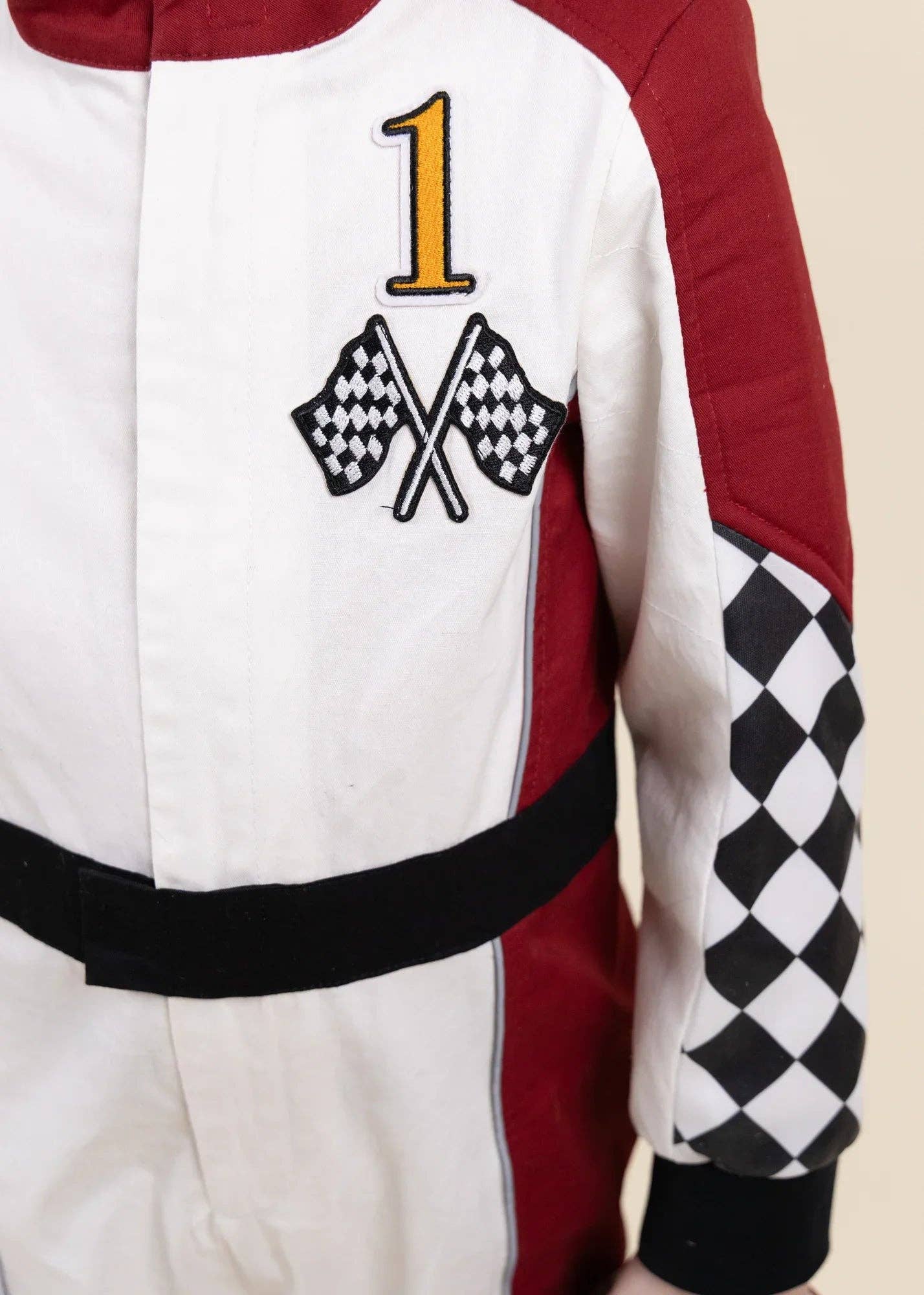 A close-up of a racing-style jacket or suit with a white body, red side panels, a black waistband, and a black-and-white checkered sleeve pattern. A large embroidered number 1 sits above crossed checkered flags on the chest.
