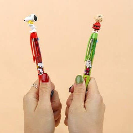 Two pens with cartoon character designs held by hands against a beige background