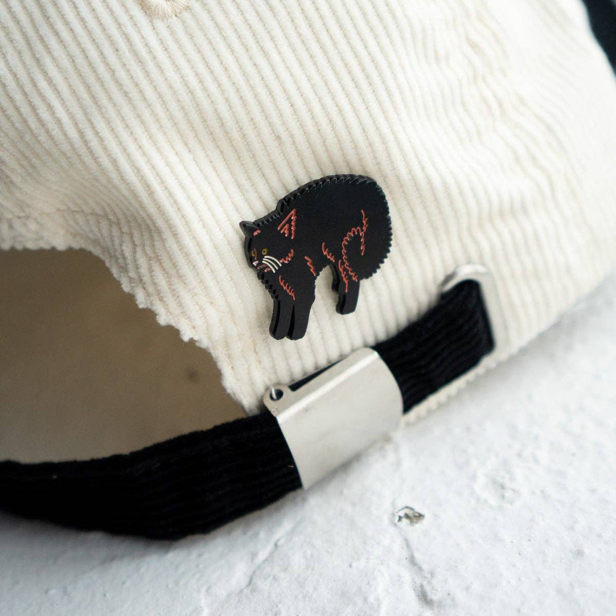 White cap with black cat patch and black strap on a white background