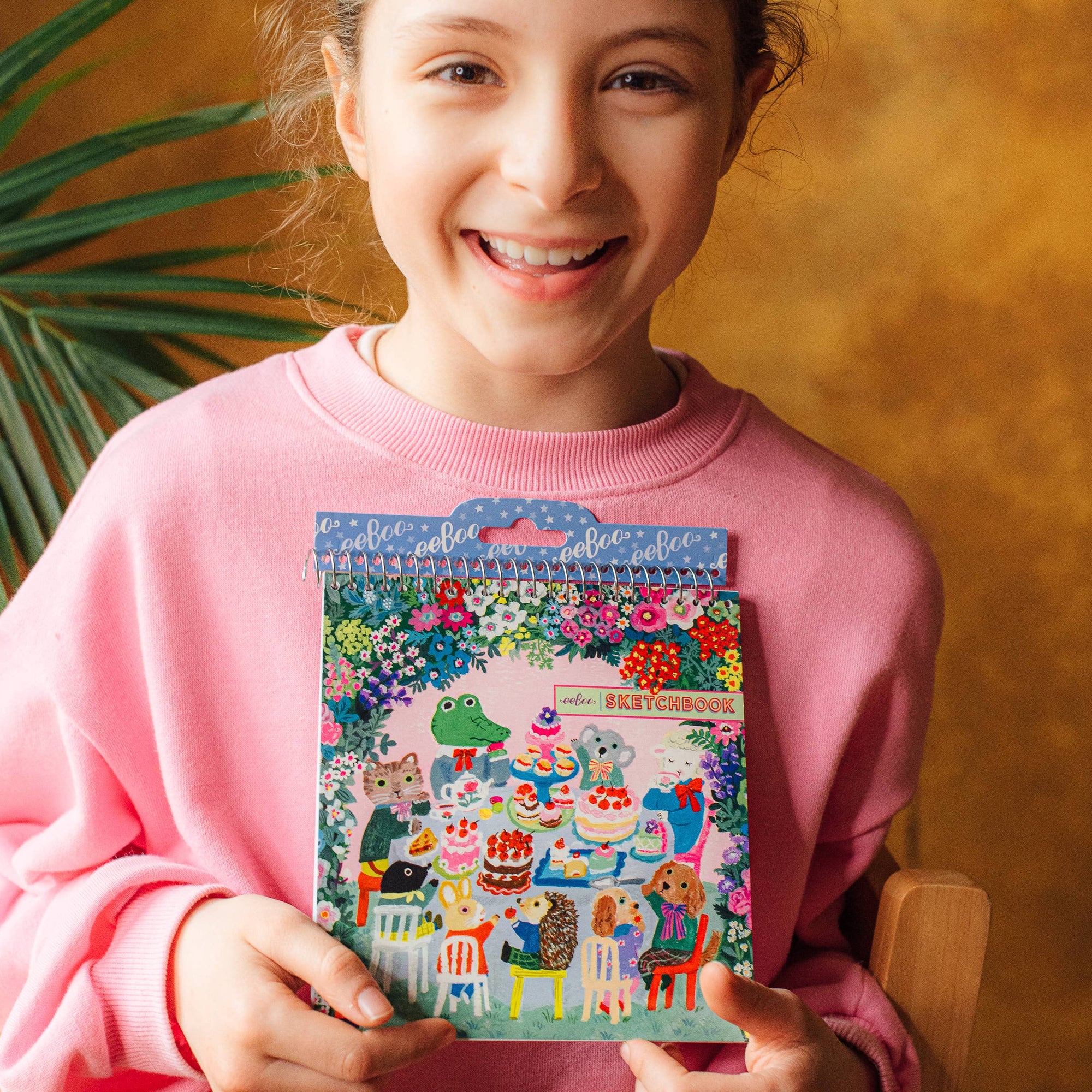 Girl holding a colorful calendar with a floral and animal design against a warm-toned background.