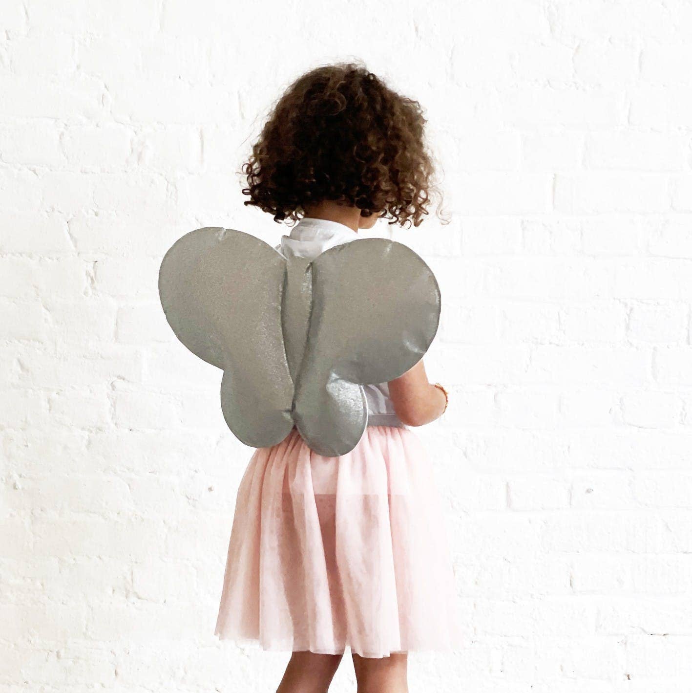 Child wearing gray butterfly wings against a white brick wall.