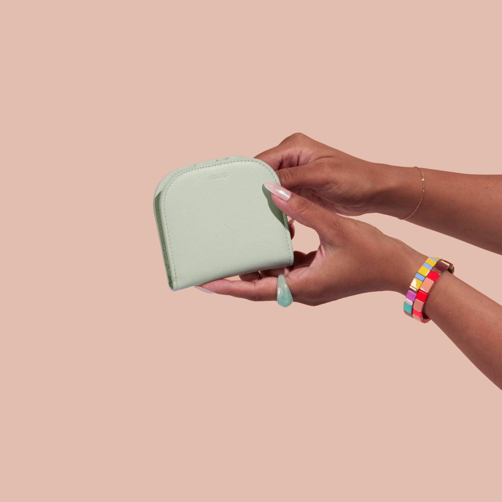 Person holding a light green wallet against a beige background