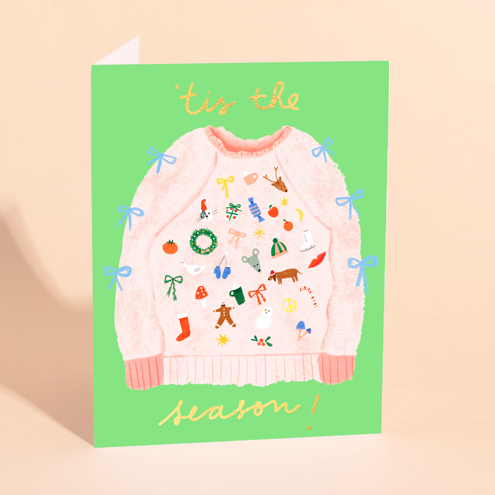 Greeting card with a pink sweater illustration and 'tis the season text on a green background