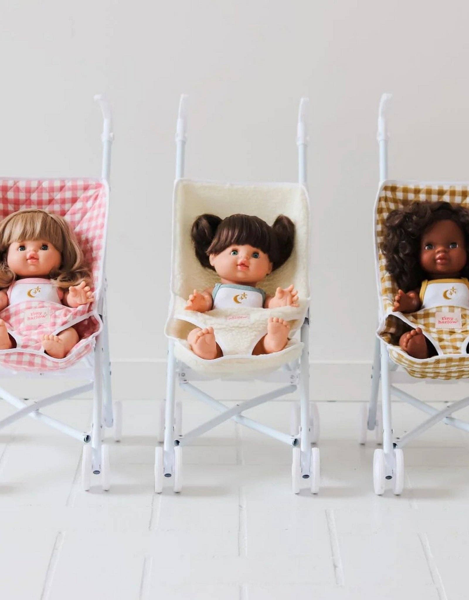 Three dolls sitting in miniature chairs with different hairstyles and outfits on a white background