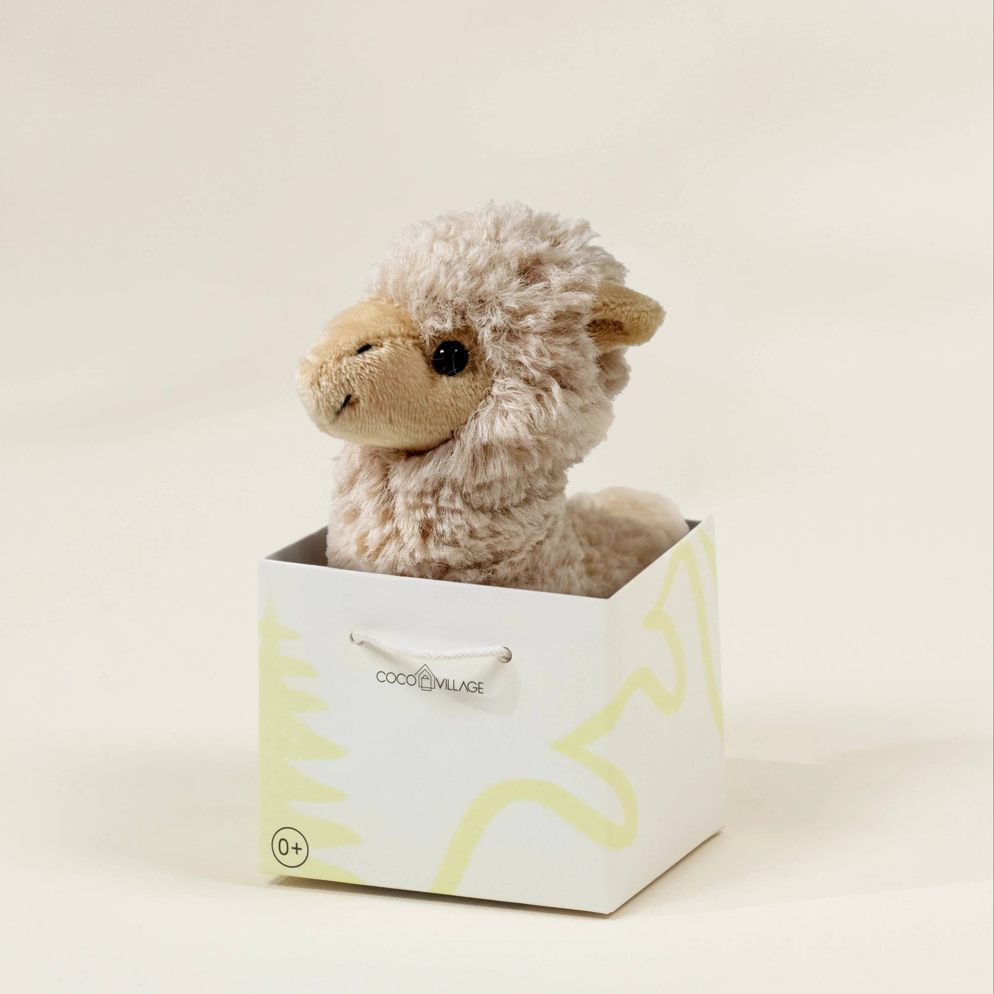 Plush toy llama in a white box with yellow patterns on a light background