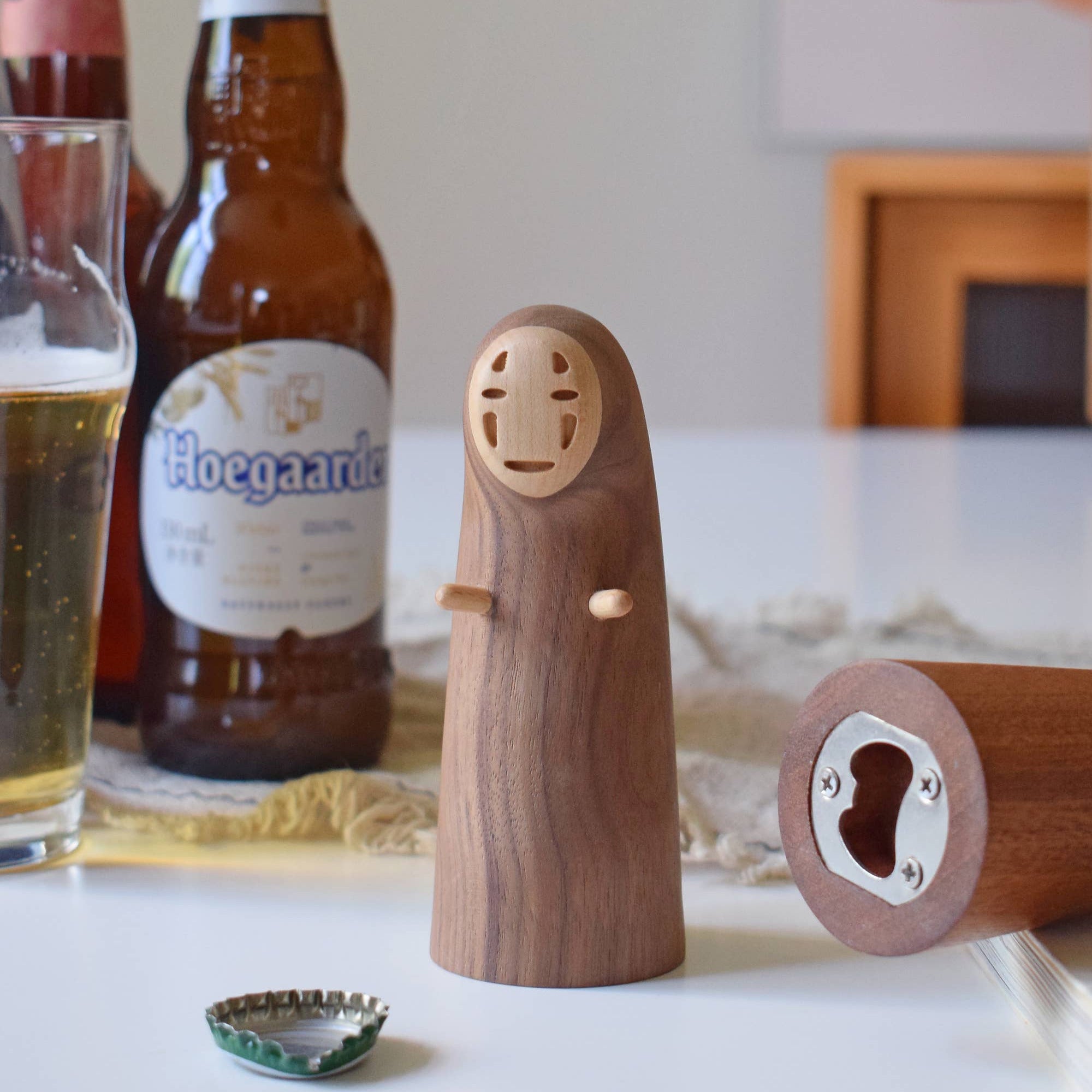 Wooden bottle opener shaped like a face with a beer bottle and glass in the background.