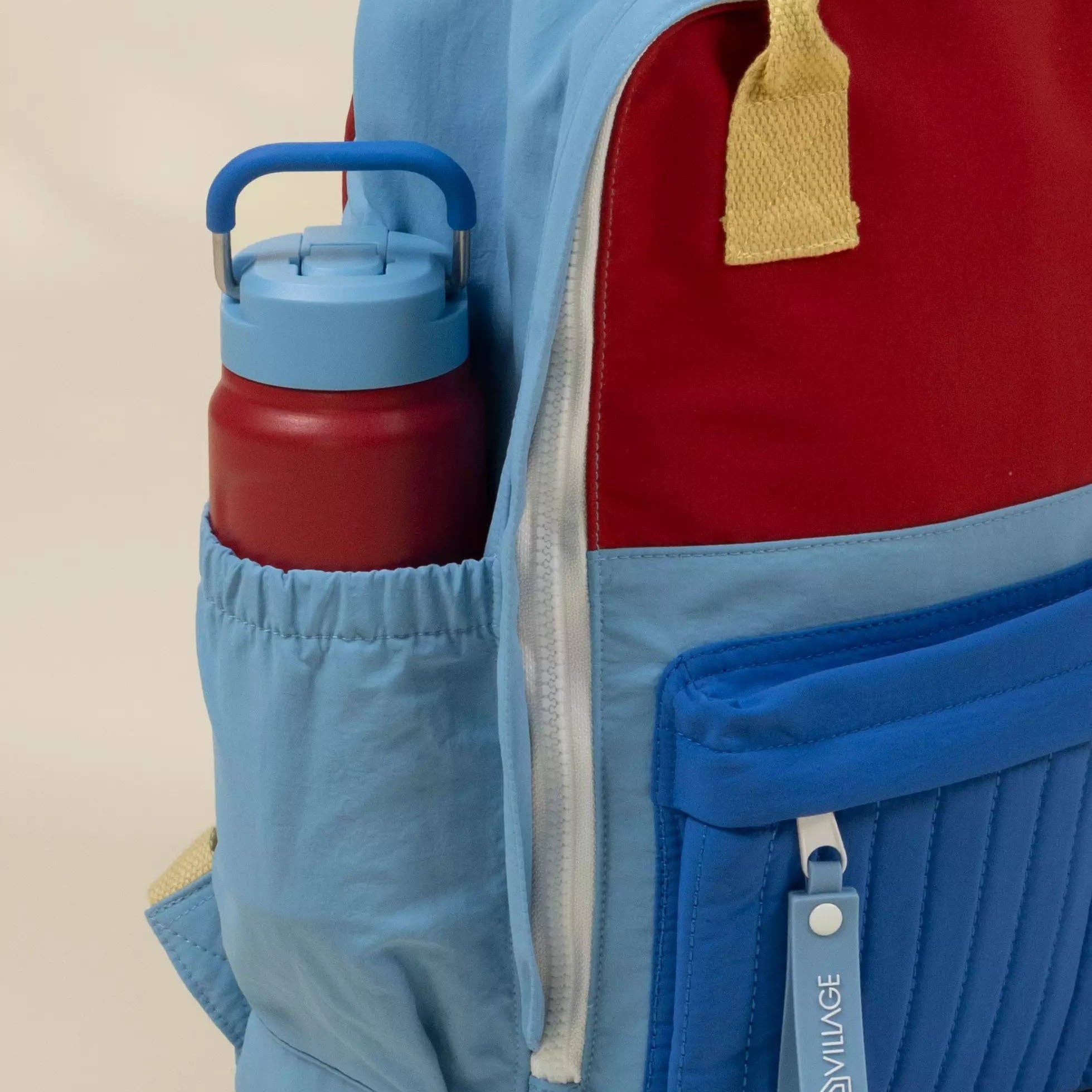 Colorful backpack with a water bottle in a pocket on a beige background