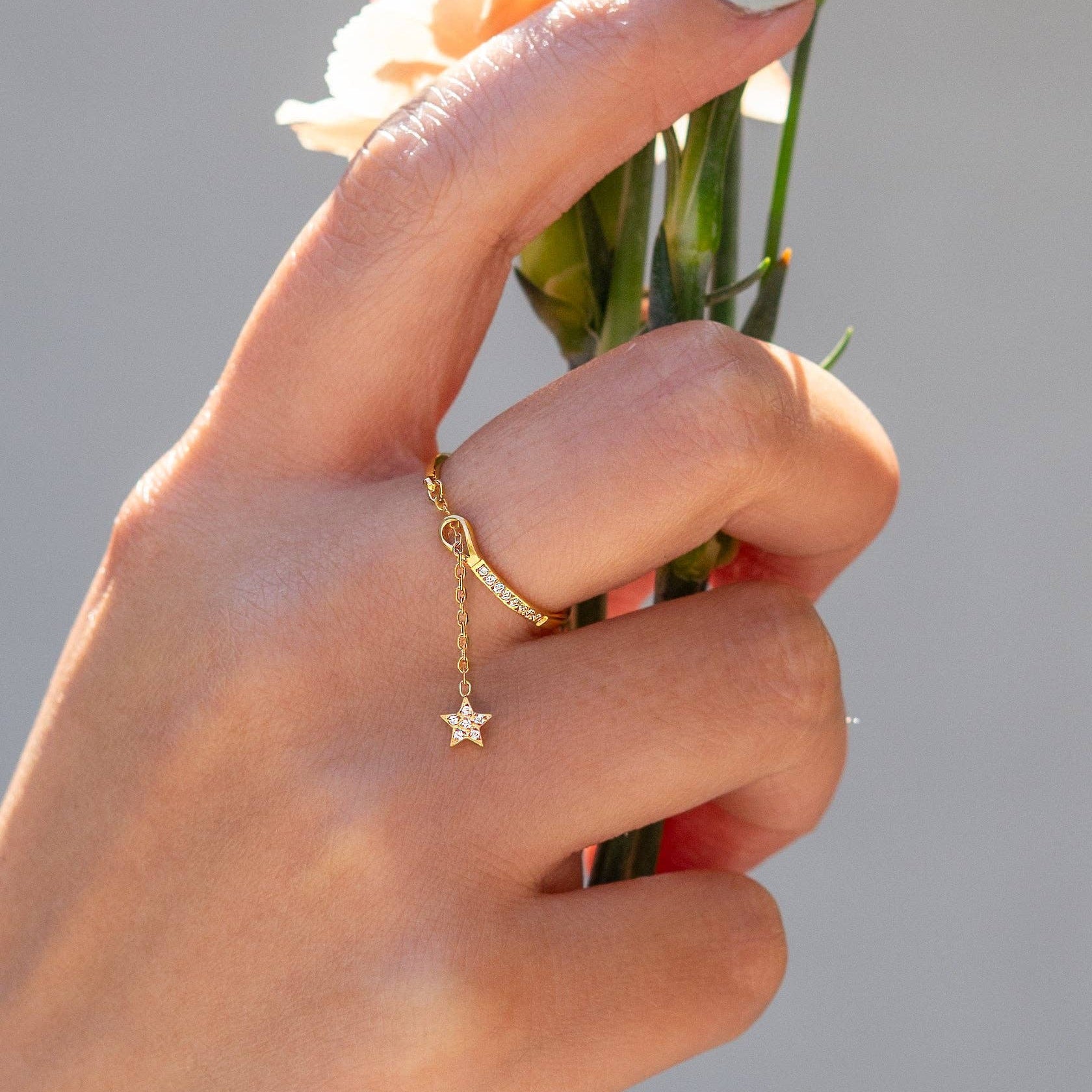 Hand holding a small bouquet of flowers with a gold ring featuring a star pendant on a neutral background