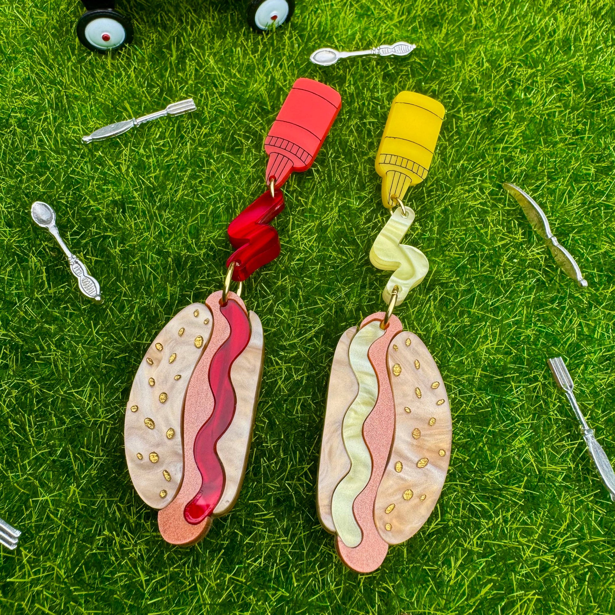 Hot dog-shaped earrings on grass with a toy wagon in the background